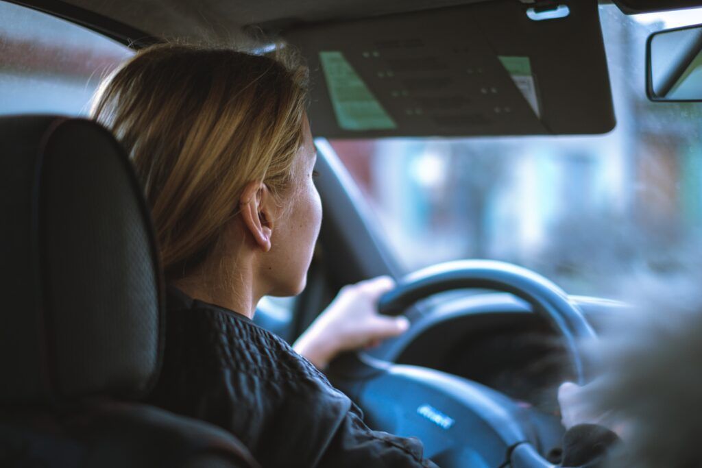 Driver seen from behind steering a car, with blurred city lights ahead
