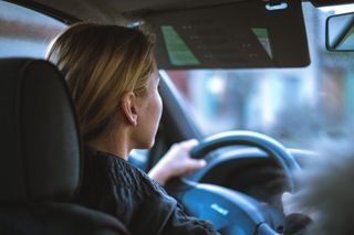 Driver seen from behind steering a car, with blurred city lights ahead