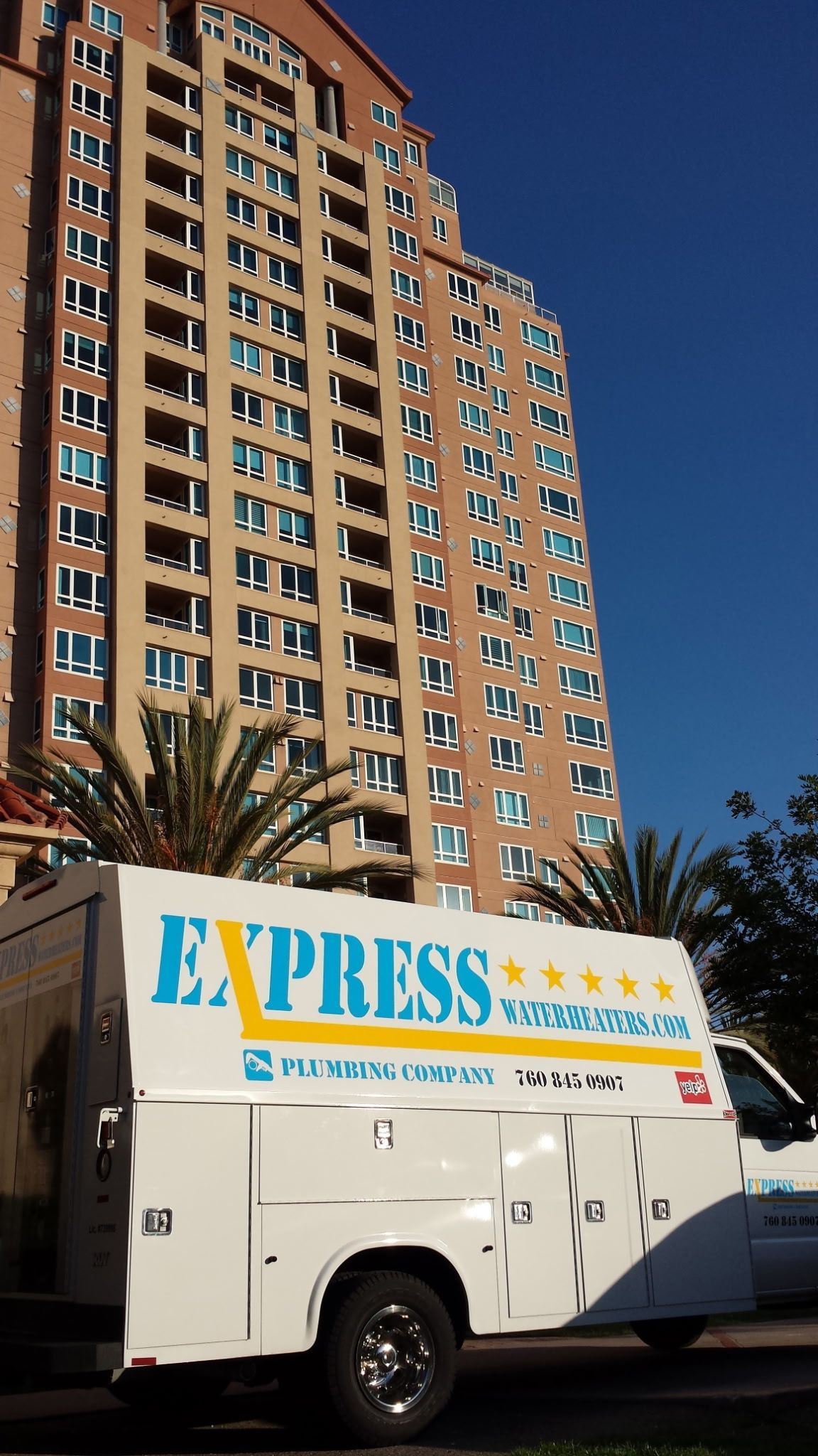 White Express moving truck parked before a tall tan apartment building under a clear blue sky