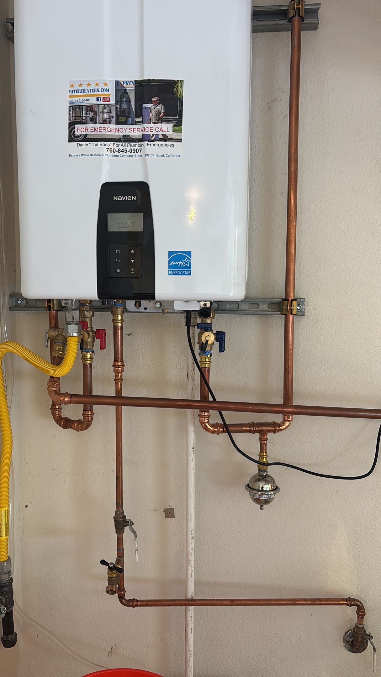 Wall-mounted white water heater with exposed copper pipes and gas line in a utility room.