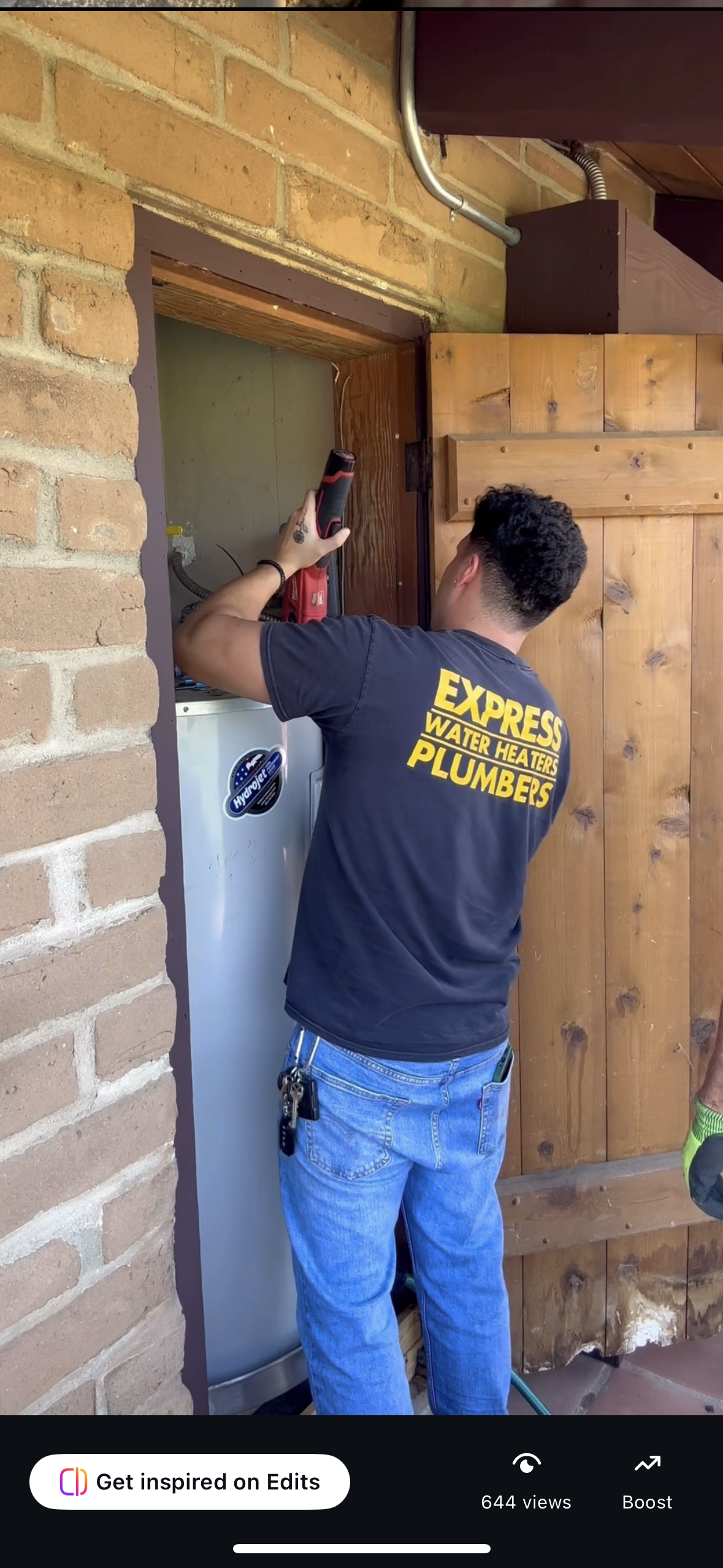 Person installing a wooden door frame beside a white refrigerator under a brick and wood awning