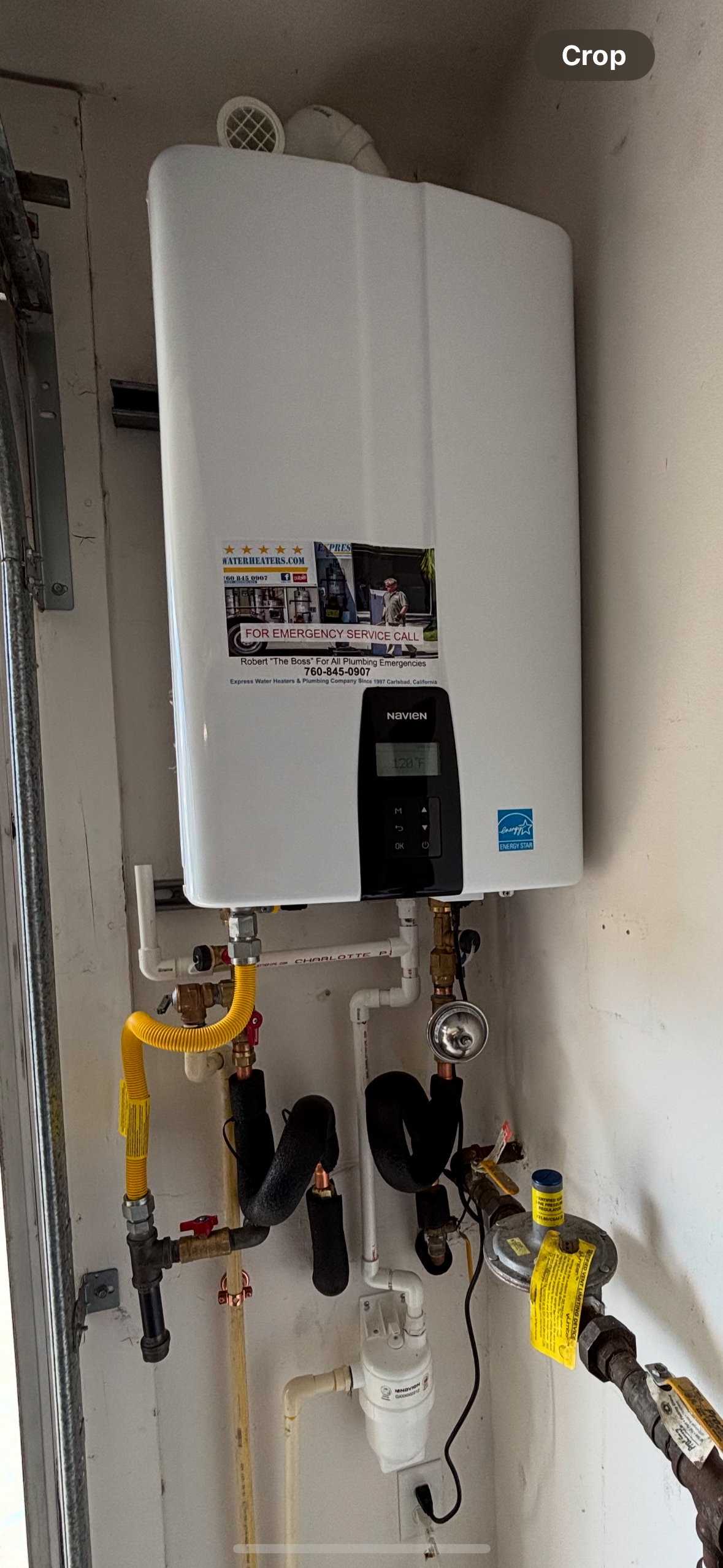 Wall-mounted white gas water heater with yellow and black pipes in a utility closet