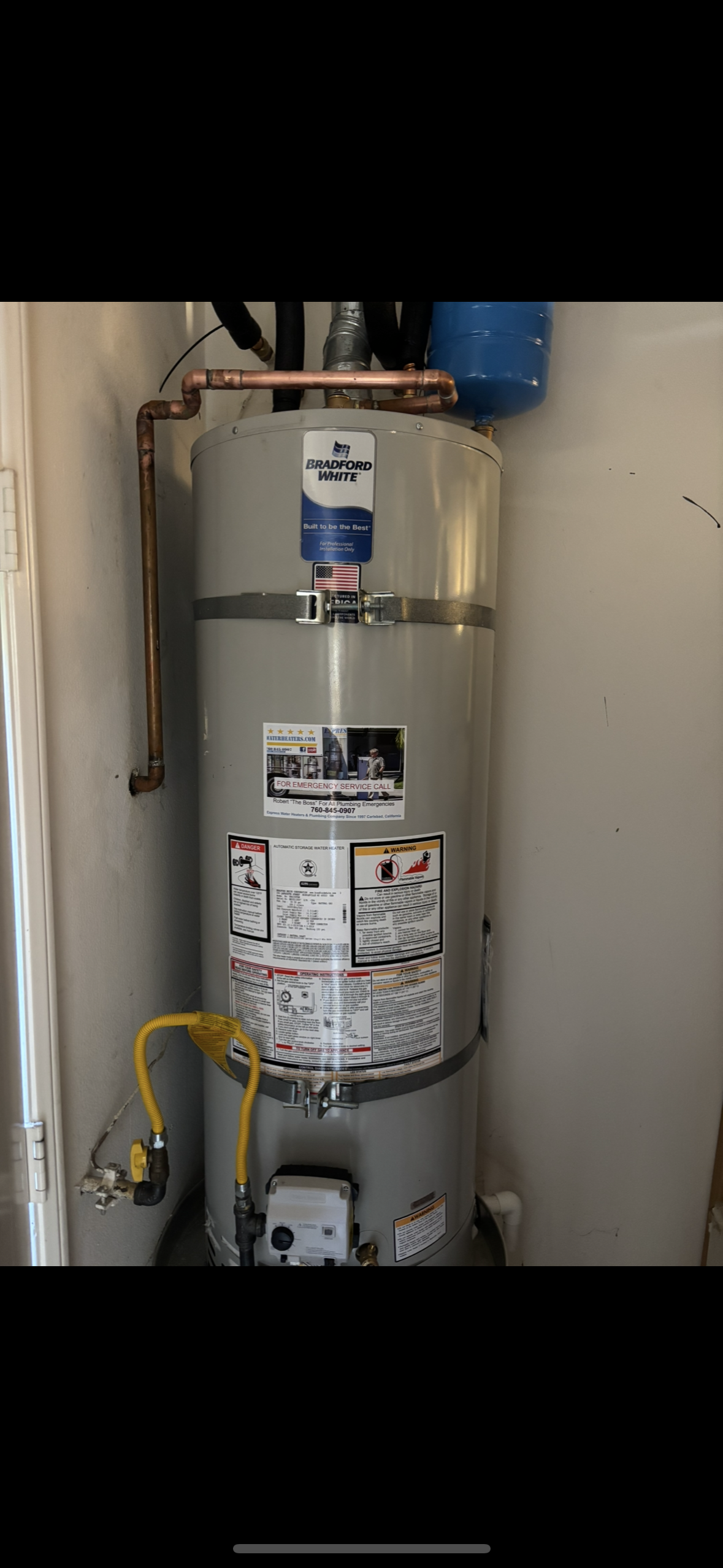 Silver water heater tank with pipes and labels in a utility closet