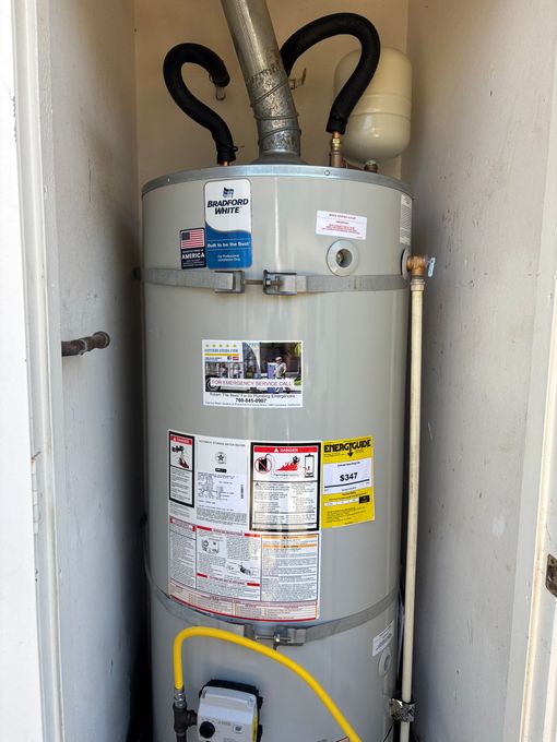 Tall gray water heater in a closet with pipes and labels, front view.