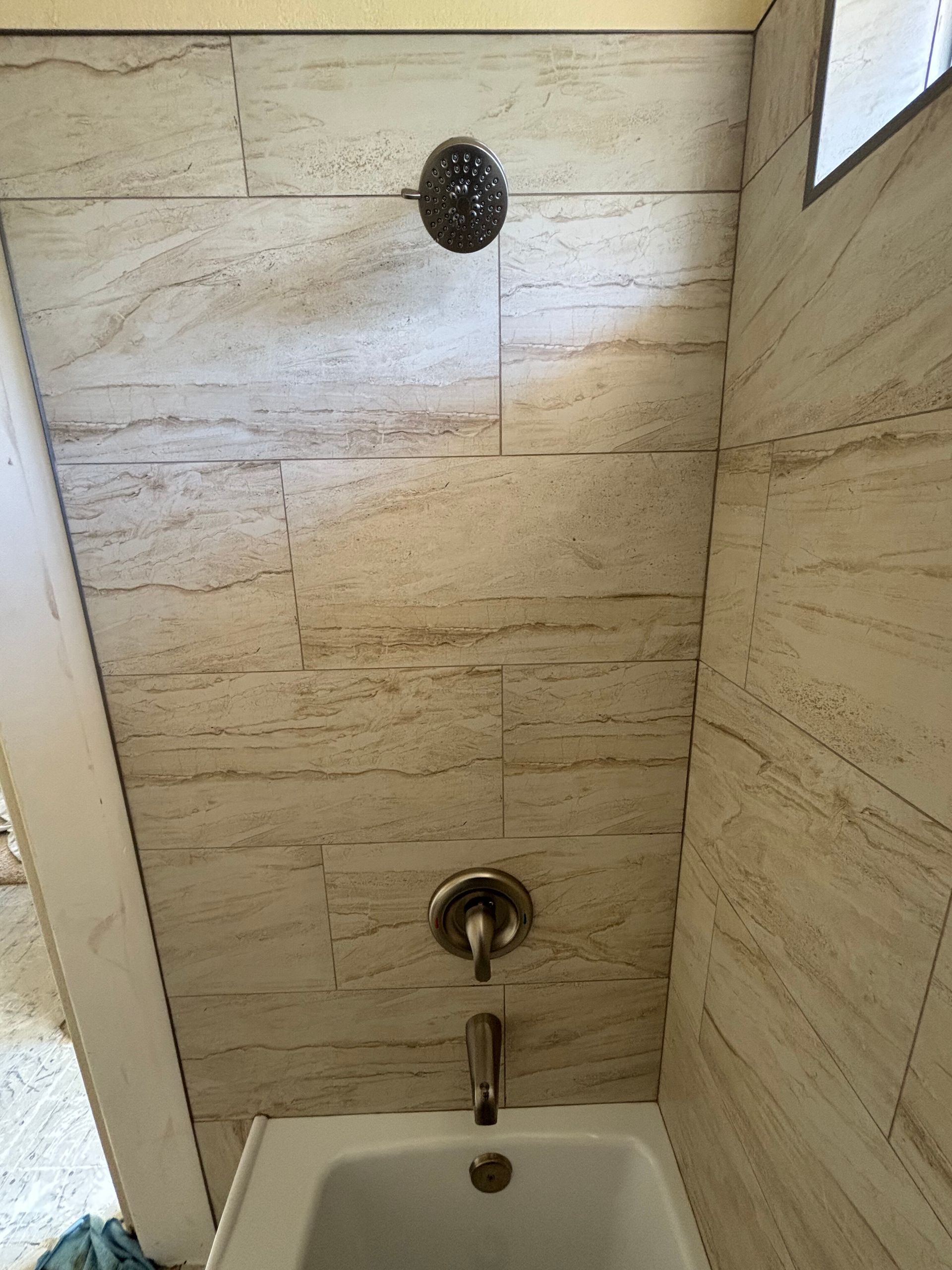 Small tiled shower wall with a round showerhead, faucet, and tub spout above a drain.