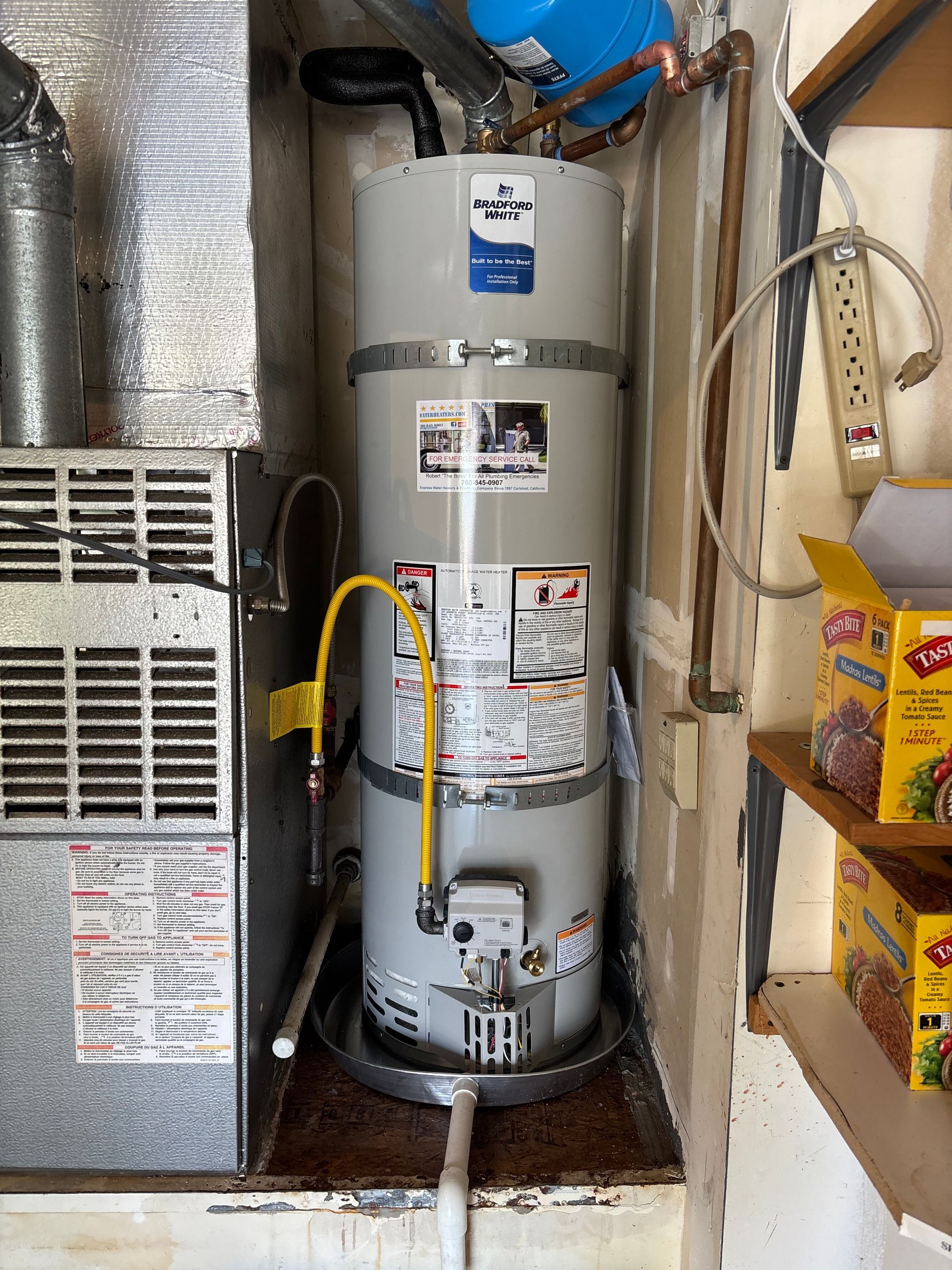 Water heater in a utility closet beside HVAC equipment and stacked boxes.