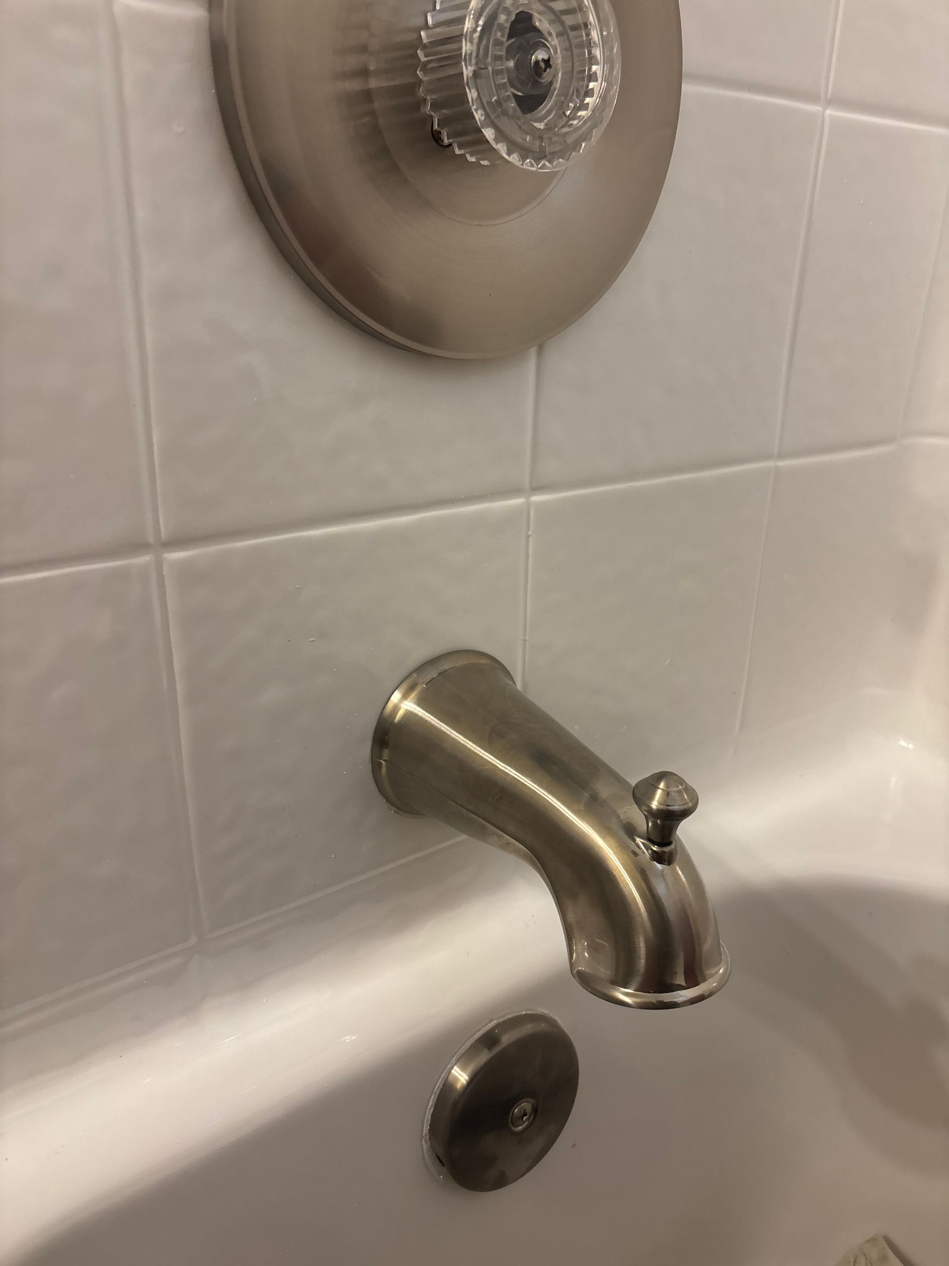Chrome bathtub faucet and drain on white tiled shower wall