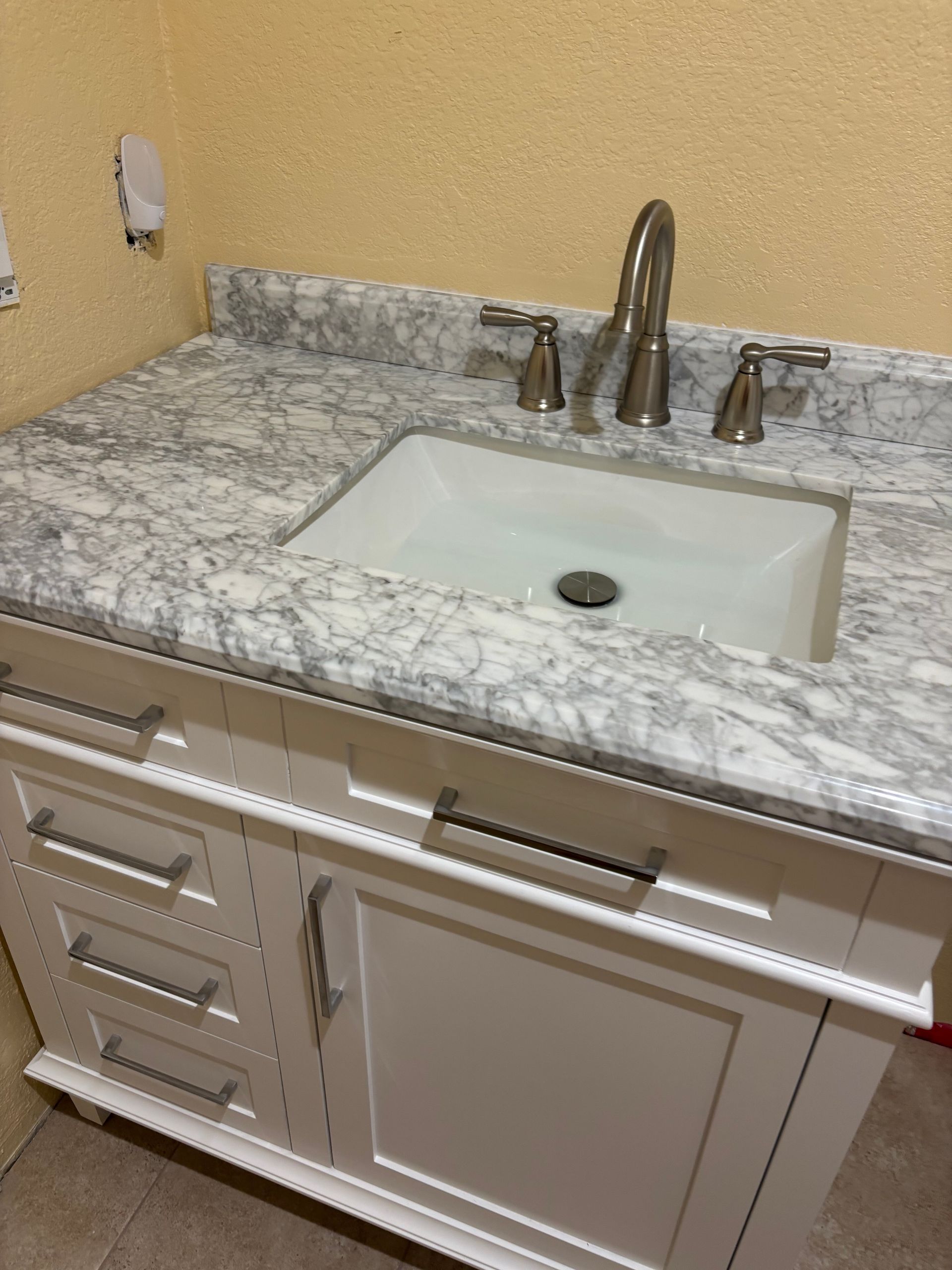 Bathroom vanity with white sink, marble countertop, and chrome faucet against a beige wall