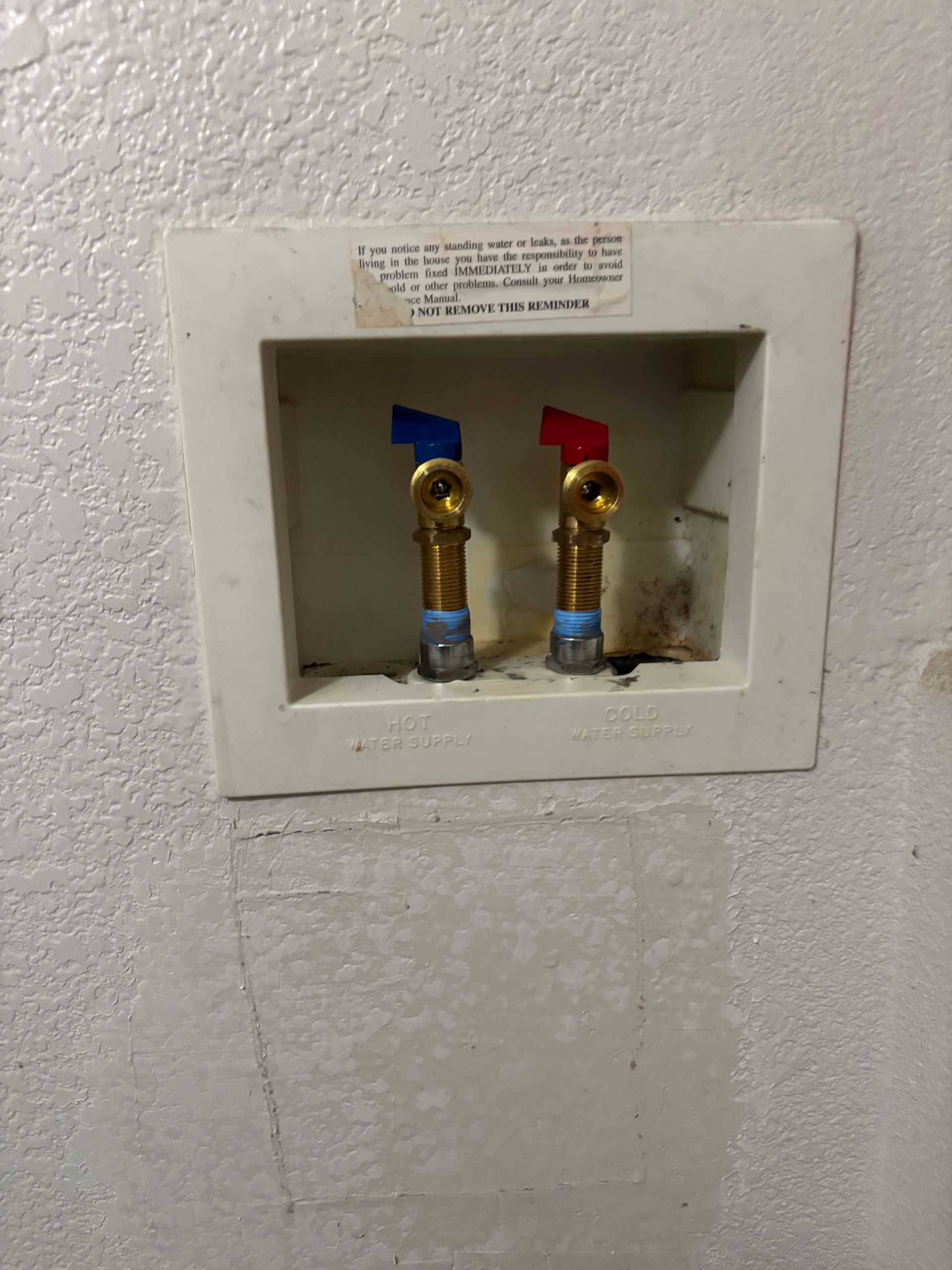 Wall plumbing access panel with two brass shutoff valves marked blue and red on a white wall
