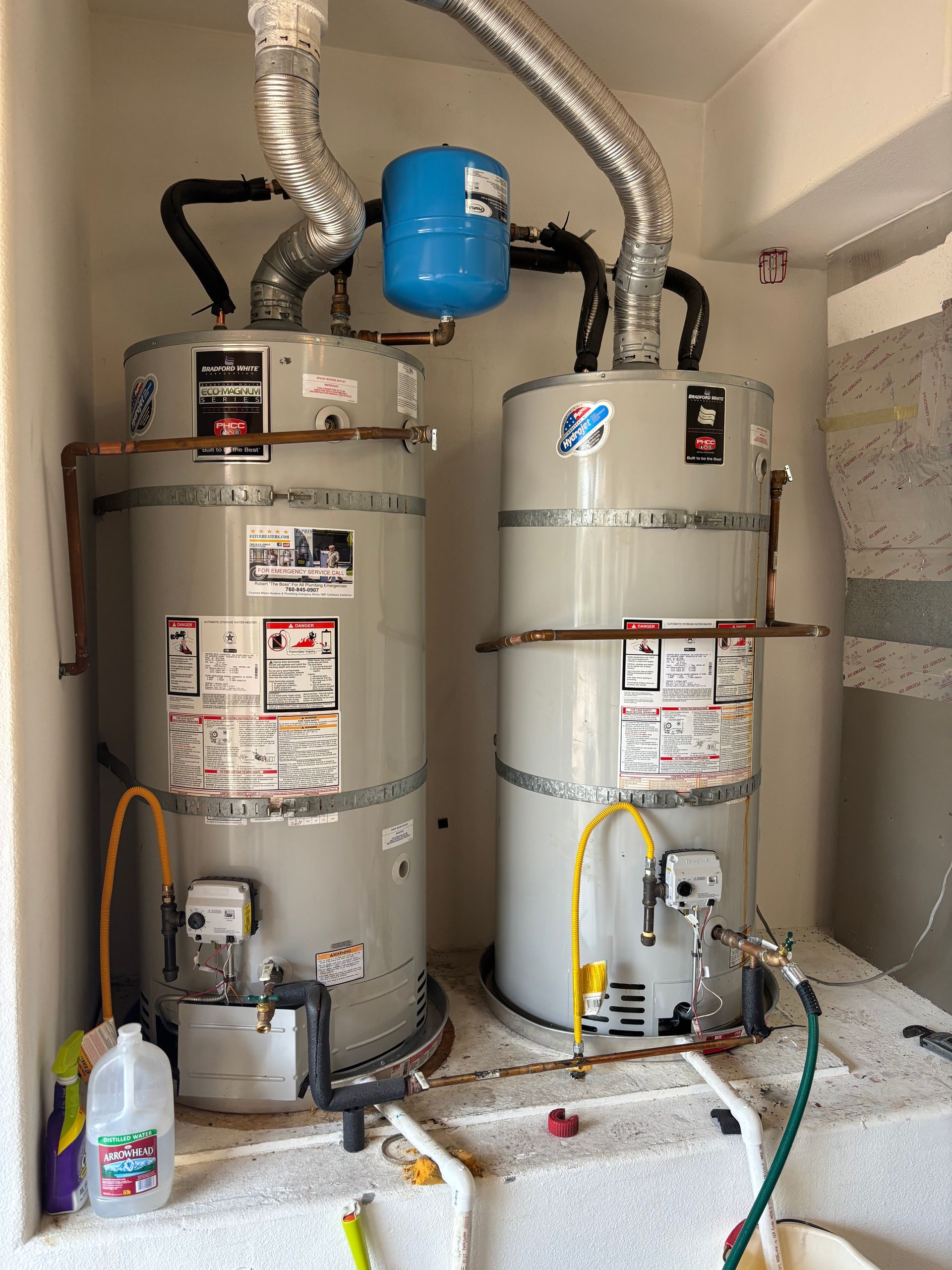 Two water heaters with vent pipes and a blue expansion tank in a utility closet