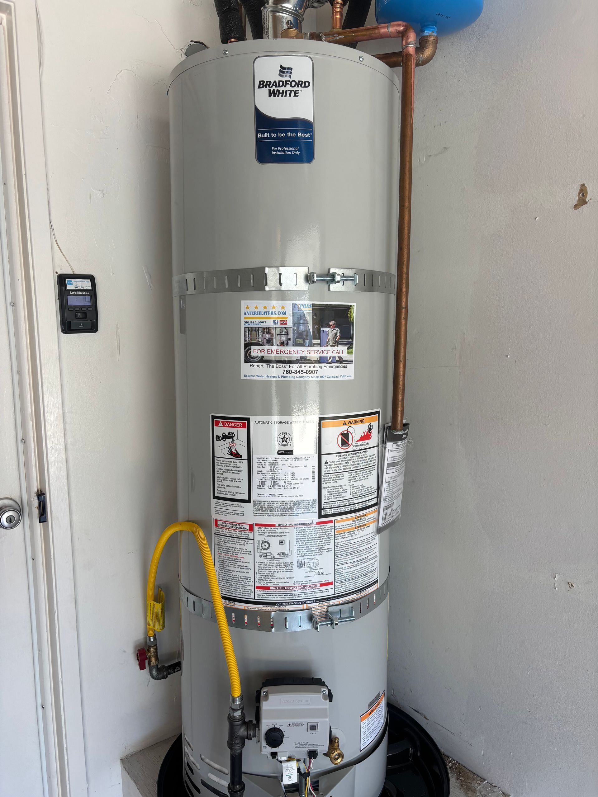 Tall gray water heater with labels and yellow gas line in a utility closet