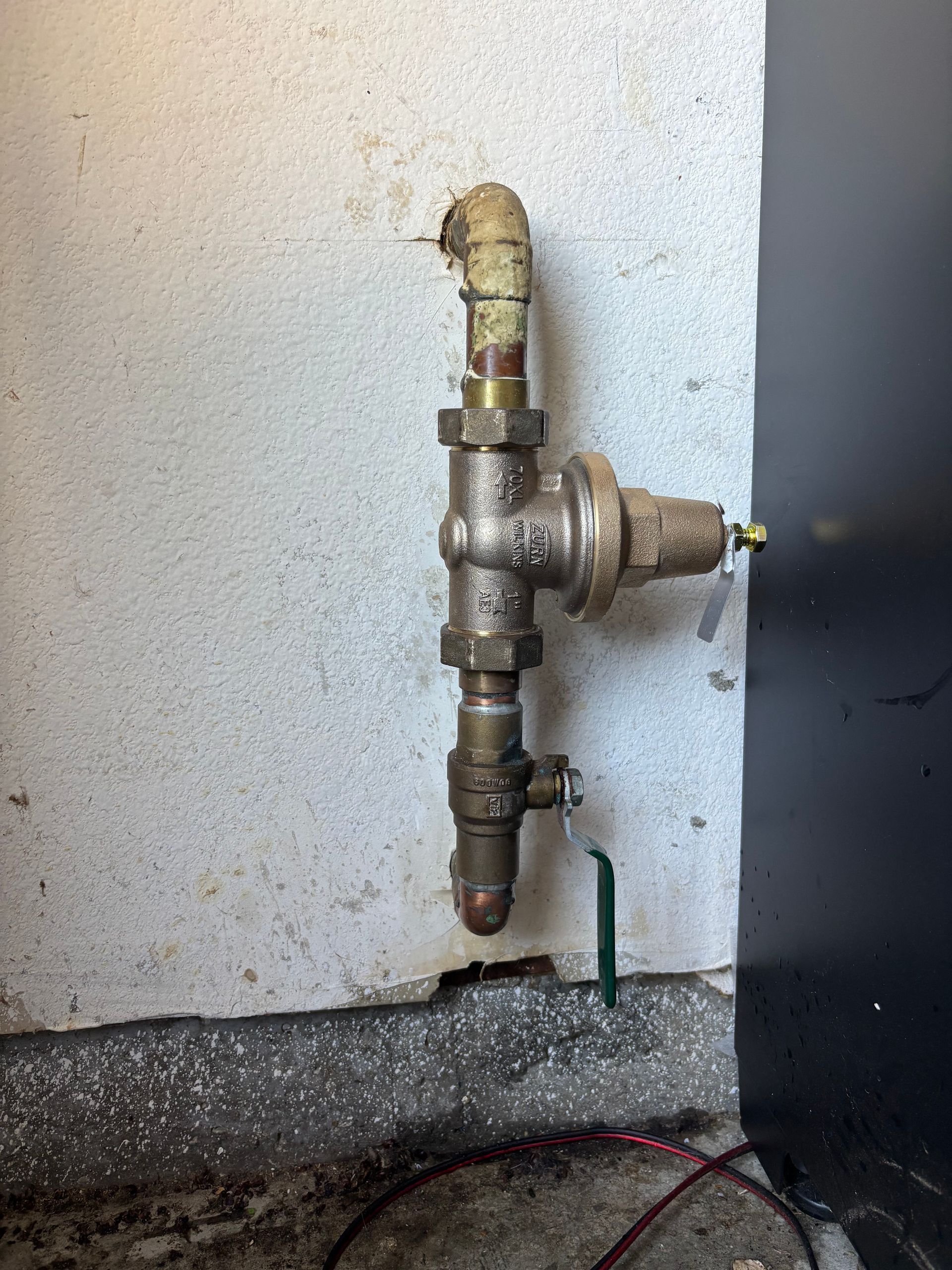 Exposed metal plumbing valve and pipe assembly on a wall near a floor baseboard