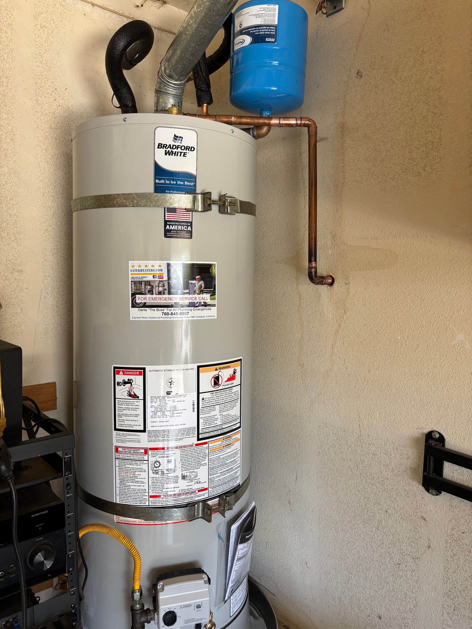 Water heater with blue expansion tank and copper pipe in a utility closet.
