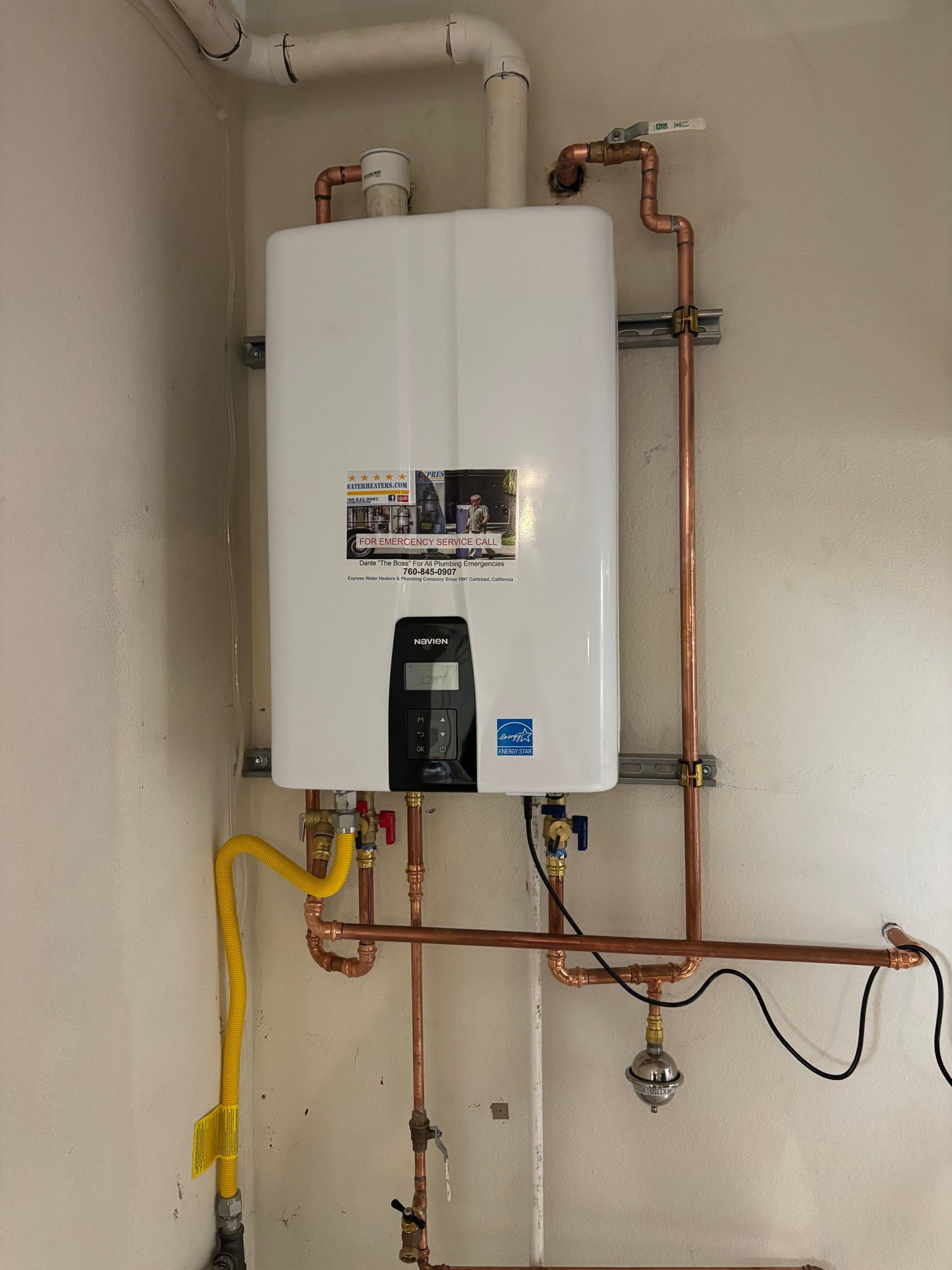 Wall-mounted white boiler with exposed copper and yellow pipes in a utility room