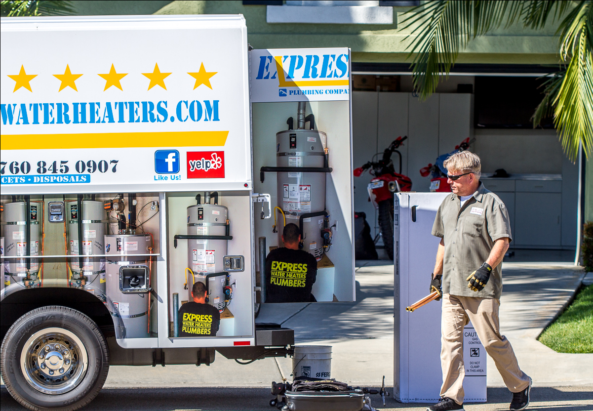 Water Heaters.com service truck beside a gas station pump with a worker standing nearby