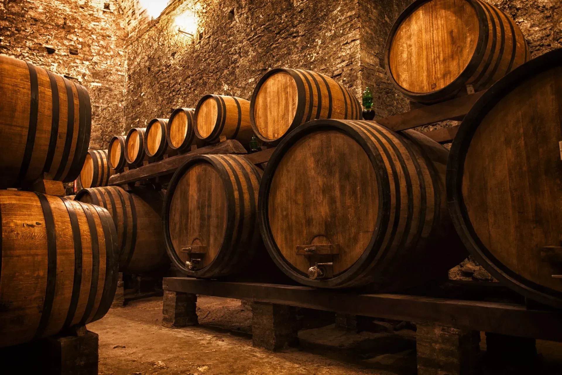 Wine barrels in a dimly lit cellar, stacked on wooden racks.