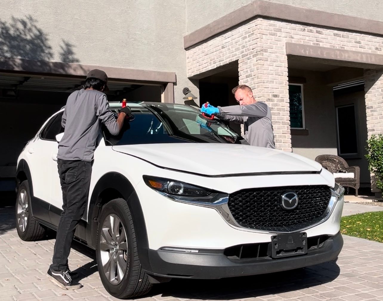 Windshield replacement with insurance on a white Mazda outside the customer's home.