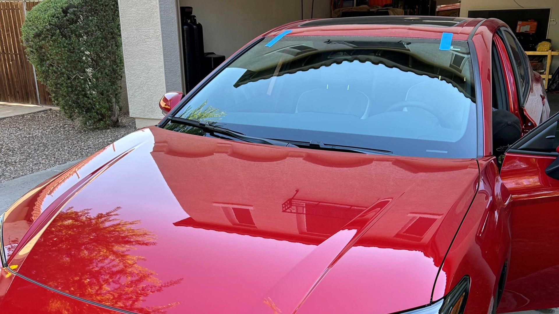 Windshield replaced on a red car with blue tape holding the windshield while urethane dries until it's safe drive away time.