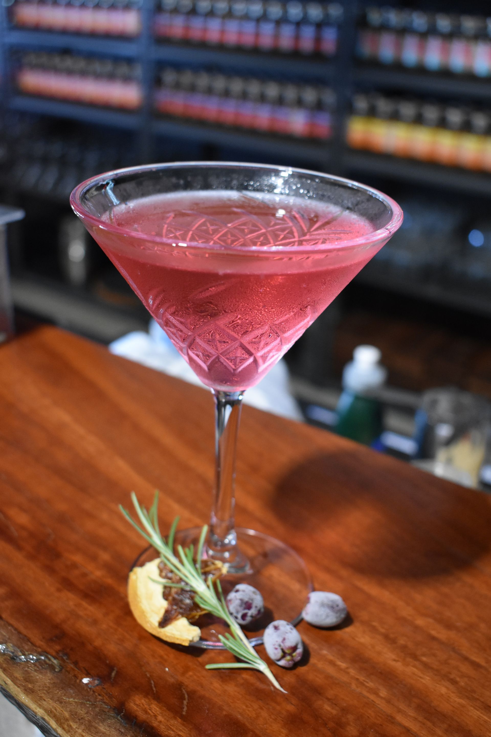 A close up of a pink cocktail in a martini glass on a wooden table.