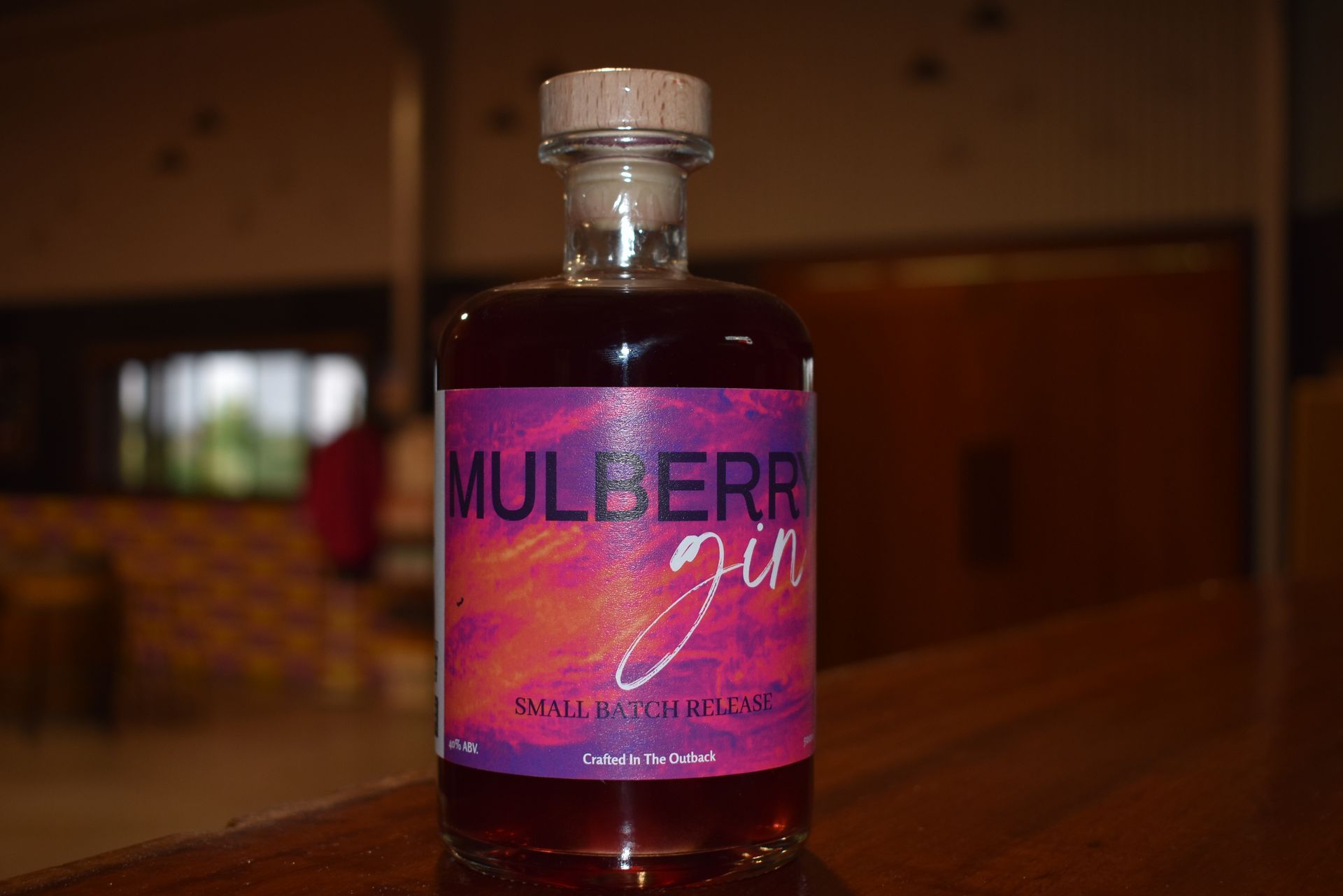 A bottle of mulberry gin is sitting on a wooden table.