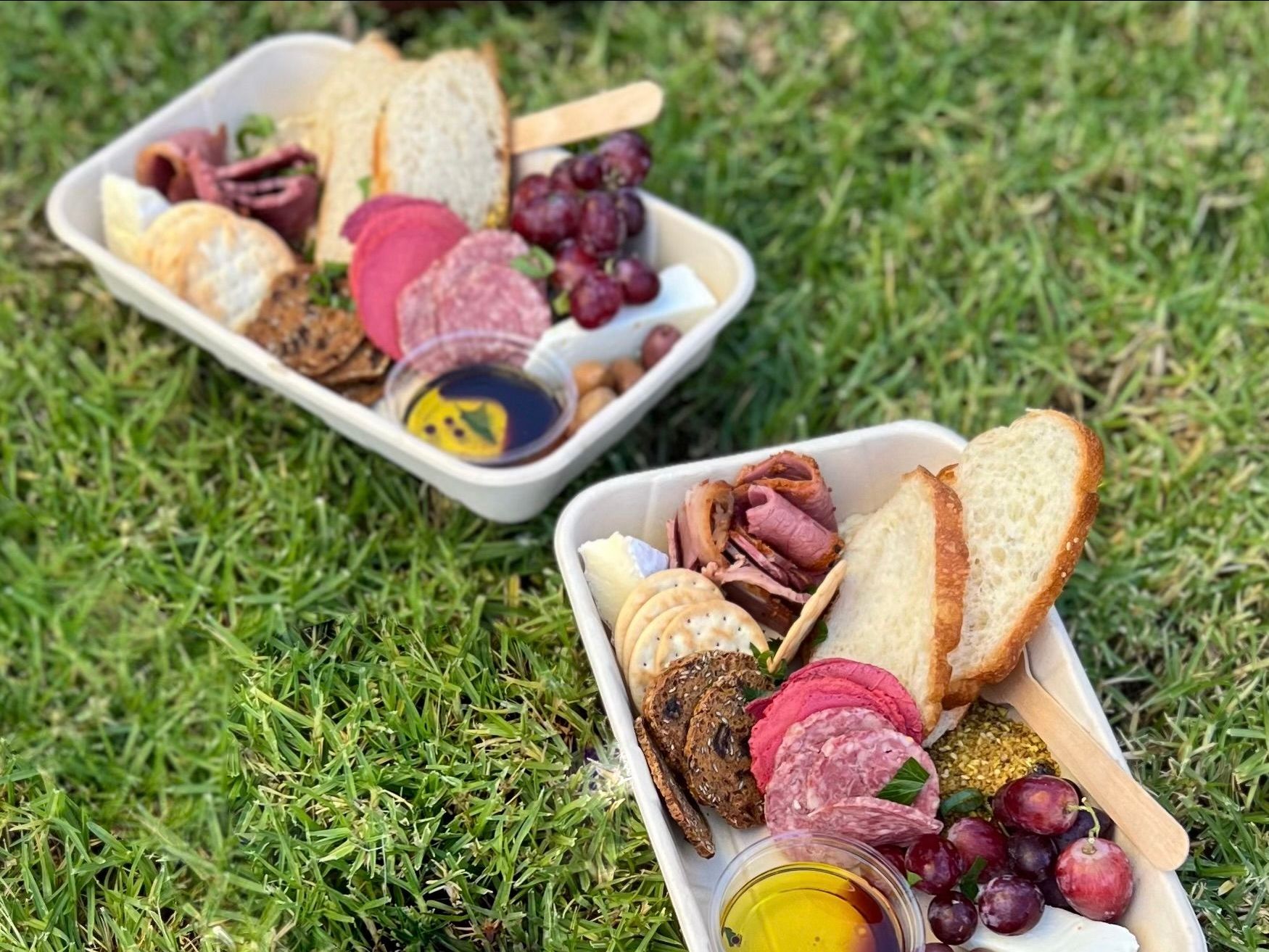 Two trays of food are sitting on top of a lush green field.