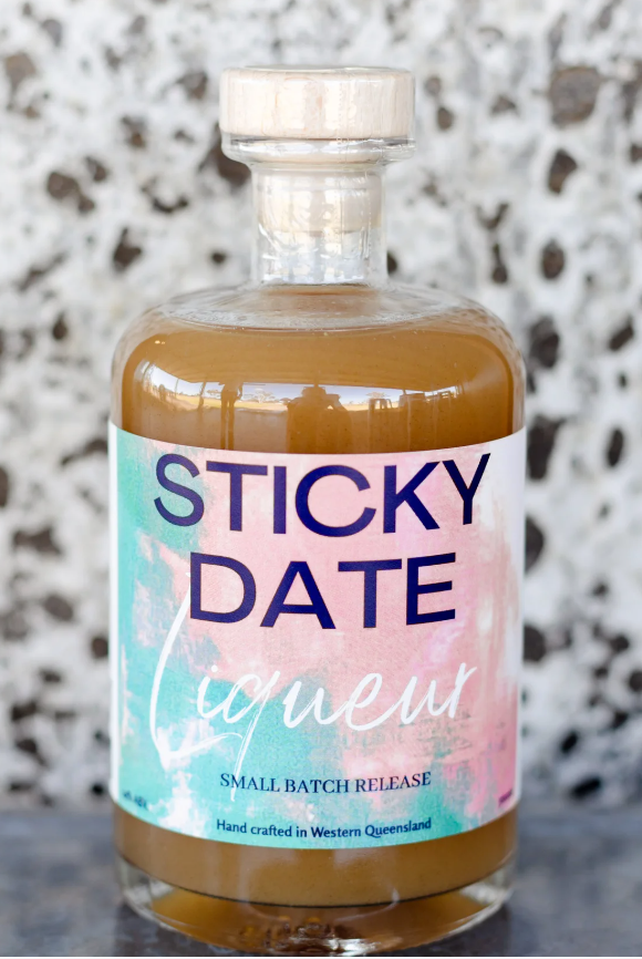 A bottle of Sticky Date Liqueur sitting on a concrete bench.