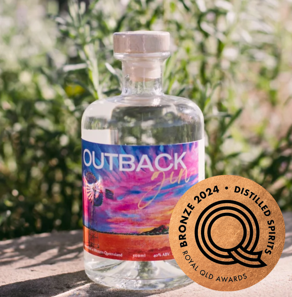 A bottle of Outback Gin sitting on a concrete surface with bushes behind it.