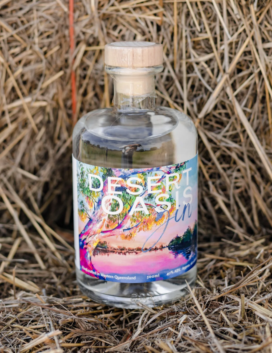 A bottle of desert oasis gin is sitting on top of a pile of hay.