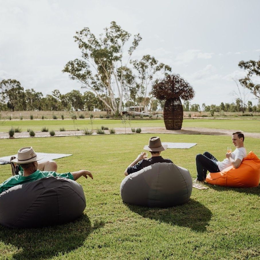 Three men are sitting on bean bag chairs in the grass.
