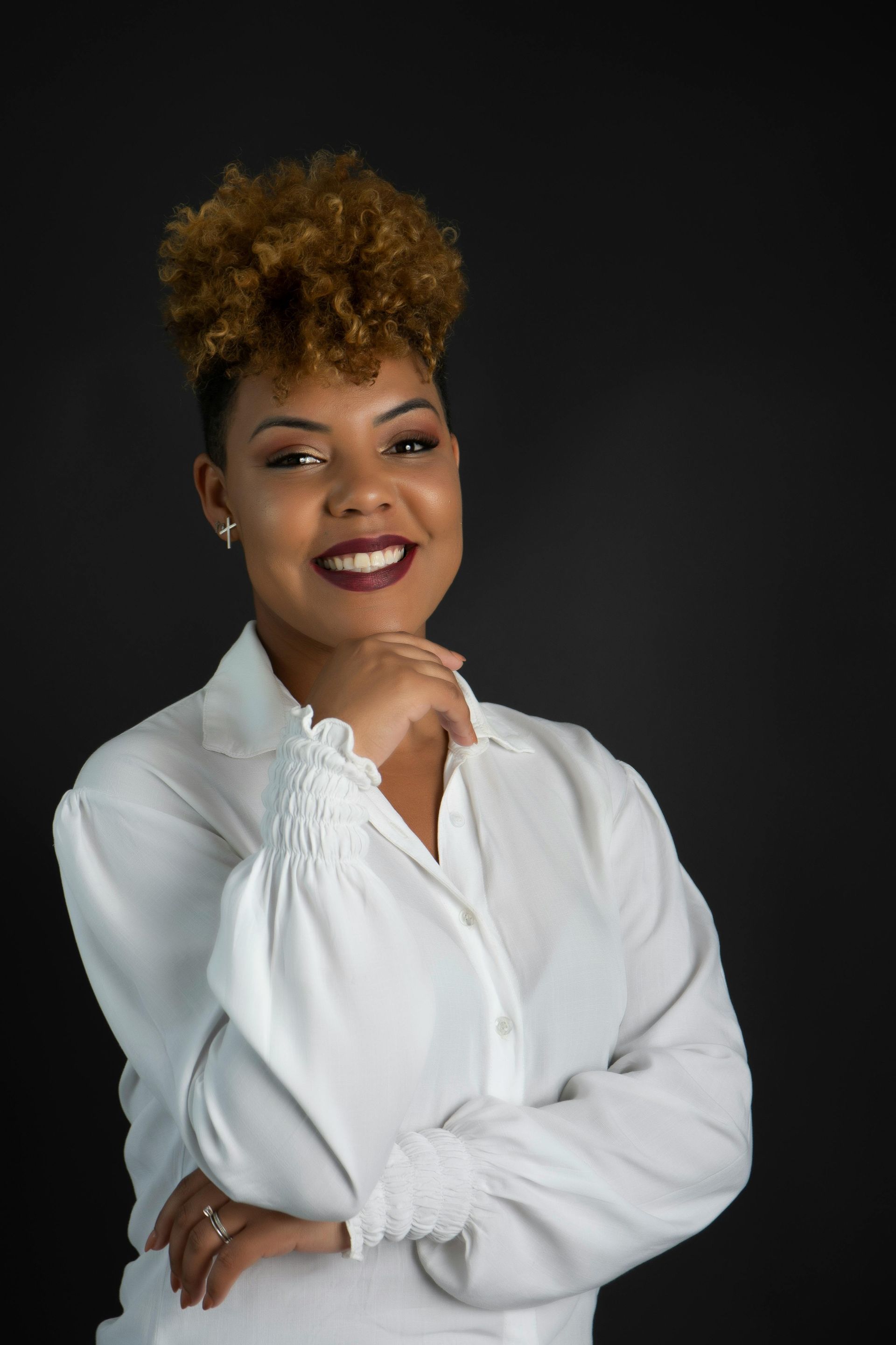 A woman in a white shirt is standing with her arms crossed and smiling for professional headshot.