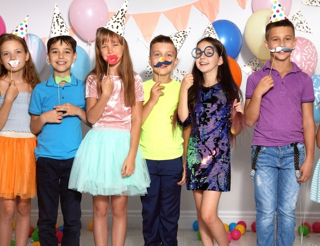 Children in party hats posing with props at a colorful birthday celebration