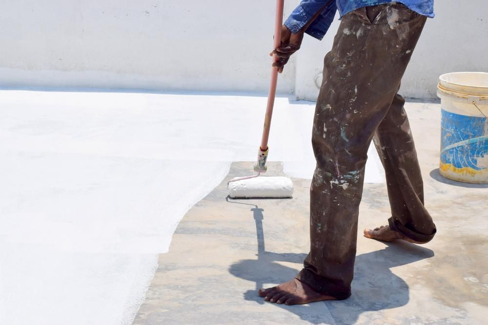 A Man Is Painting A Concrete Surface With A Roller — Paint & Trade Supplies Lismore In Ballina, NSW