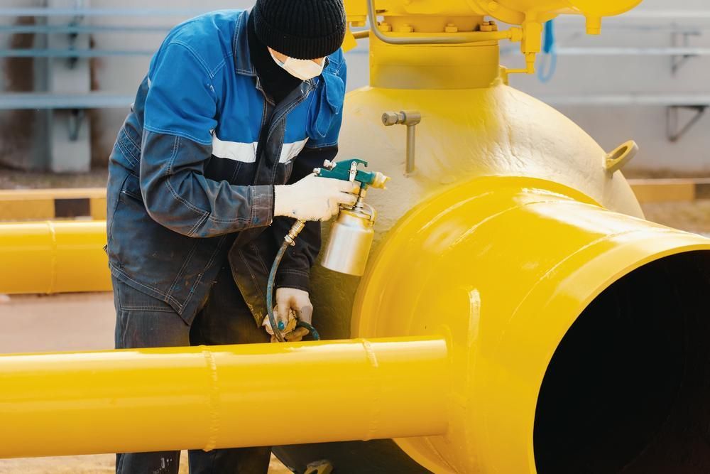 A Man Is Spraying Yellow Paint On A Yellow Pipe — Paint & Trade Supplies Lismore In Goonellabah, NSW
