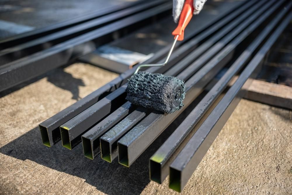 A Person Is Painting A Bunch Of Metal Bars With A Roller — Paint & Trade Supplies Lismore In Murwillumbah, NSW
