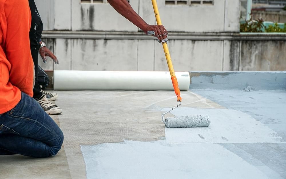 A Man Is Painting A Roof With A Roller — Paint & Trade Supplies Lismore In Goonellabah, NSW