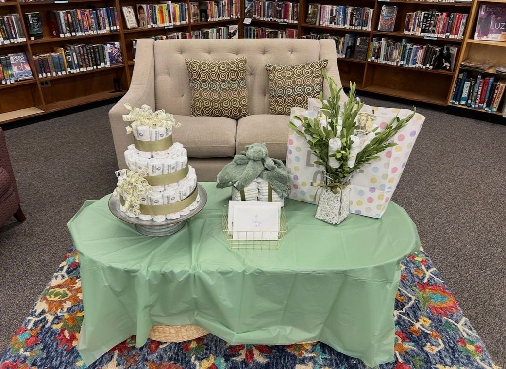 Gift table with cake, flowers, and wrapped presents in a library seating area