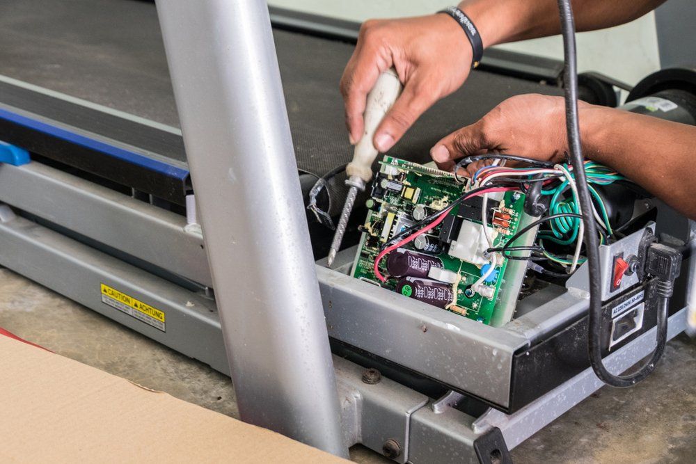 A Man is Fixing a Treadmill With a Screwdriver — Hennig Electrical Services in Buddina, QLD