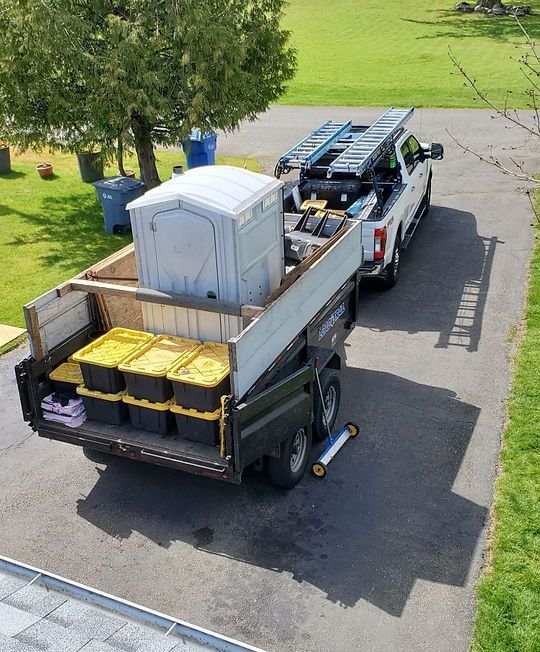 Truck bed loaded with portable toilets, tools, and yellow bins on a driveway outdoors
