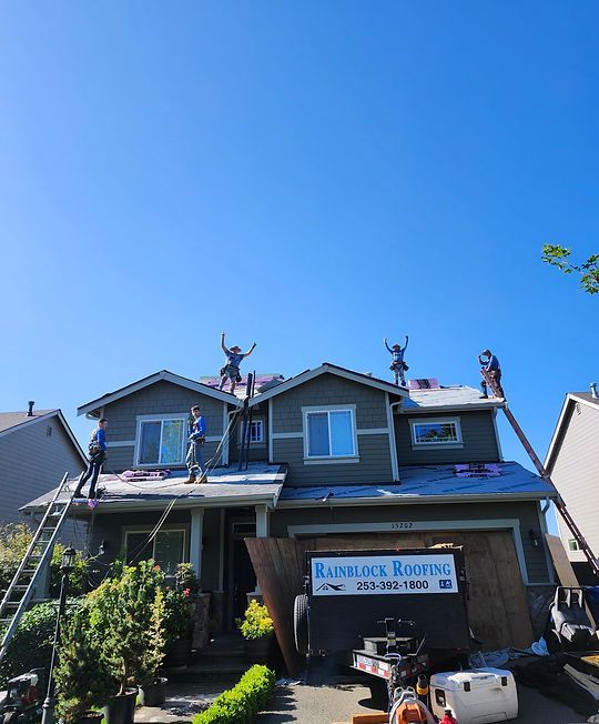 House with roofing workers on the roof under a bright blue sky, garage sign visible below