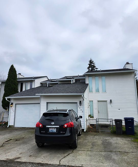Black SUV parked in front of a white two-story house with a garage on a cloudy day
