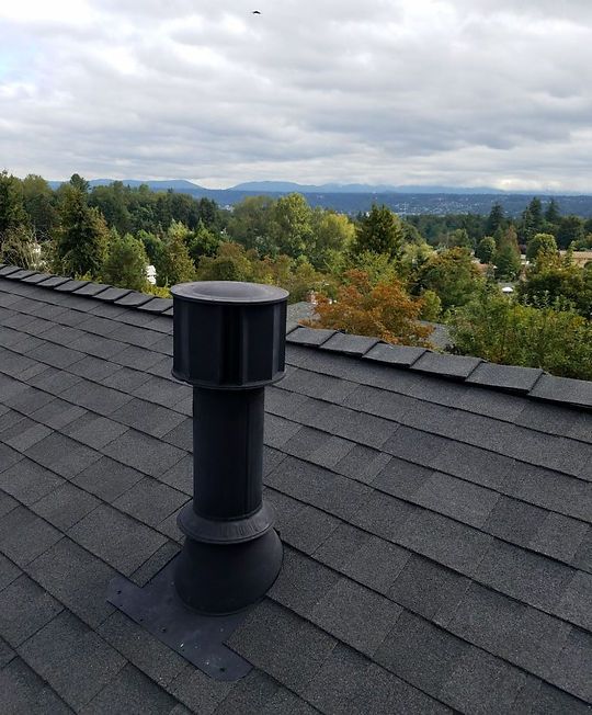 Rooftop vent on a shingled roof with trees and cloudy mountains in the background