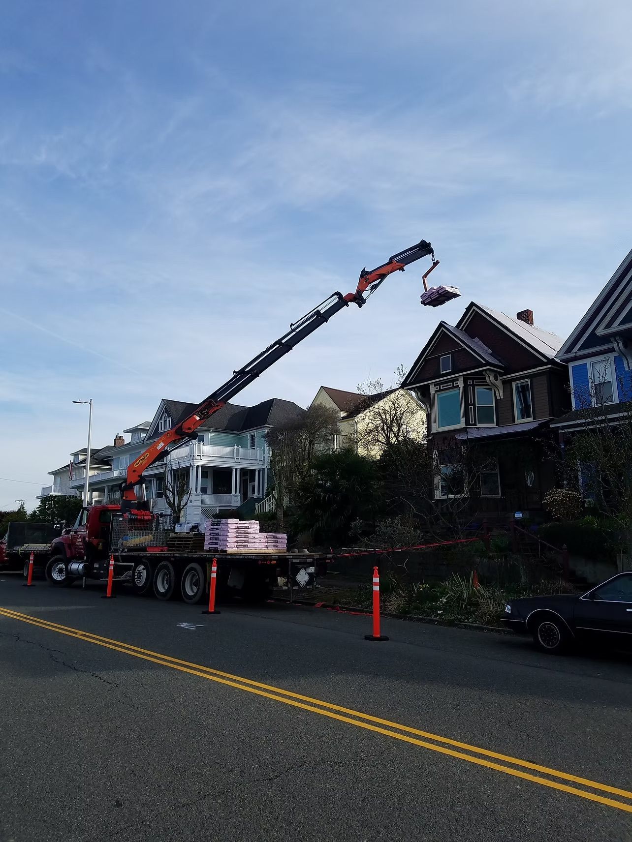 Crane truck lifting debris beside damaged houses on a residential street
