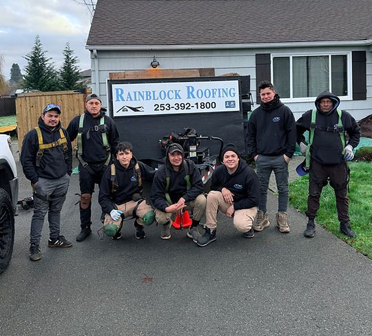 Six roofers posing outside a house beside a Rainlock Roofing sign