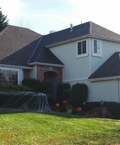 Suburban house with gray siding, dark roof, front lawn, and a sprinkler watering the yard