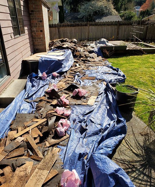 Blue tarp-covered debris piles along a side yard next to a house and fence