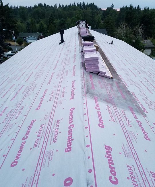 Damaged house with exposed roof; roofers work above a garage labeled “Rainbow Roofing.”