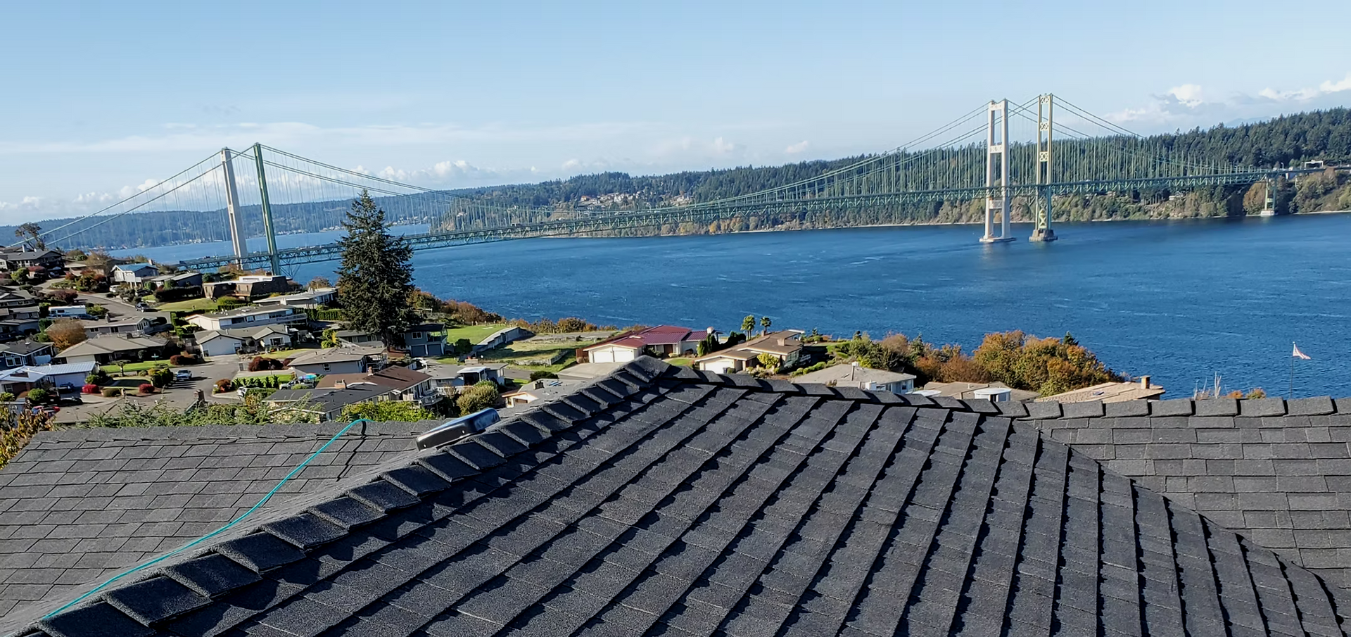 Panoramic view of a bridge over blue water with rooftops and trees in the foreground
