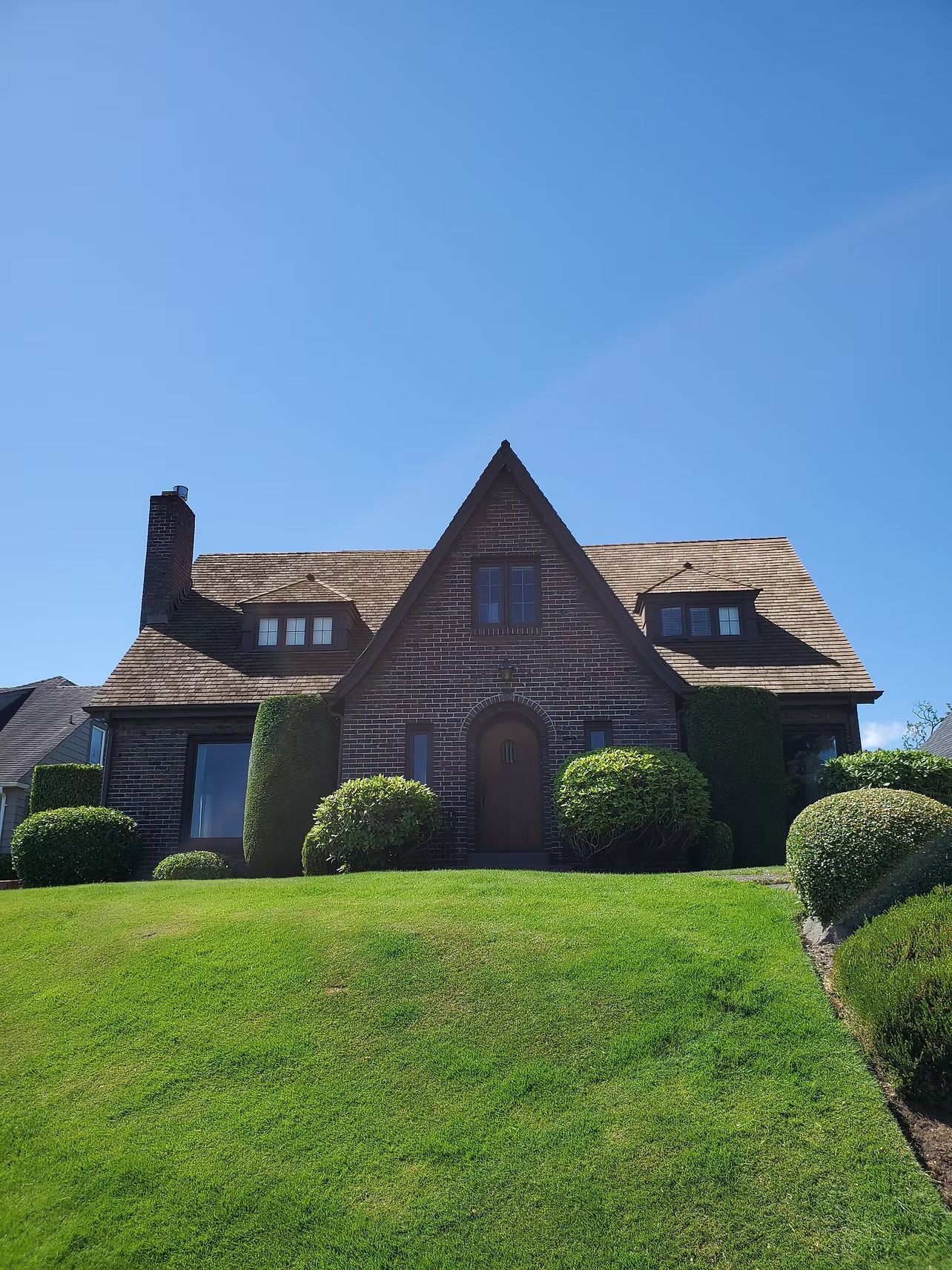 Stone house with steep roof and manicured lawn under a clear blue sky