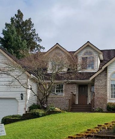 Suburban two-story brick house with a green lawn, white garage, and trees in front