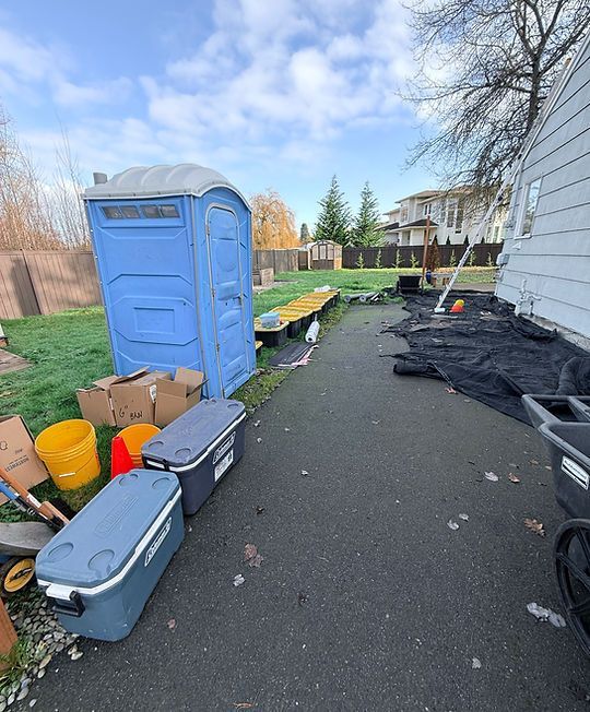 Backyard with a blue portable toilet, storage bins, and scattered yard materials beside a house